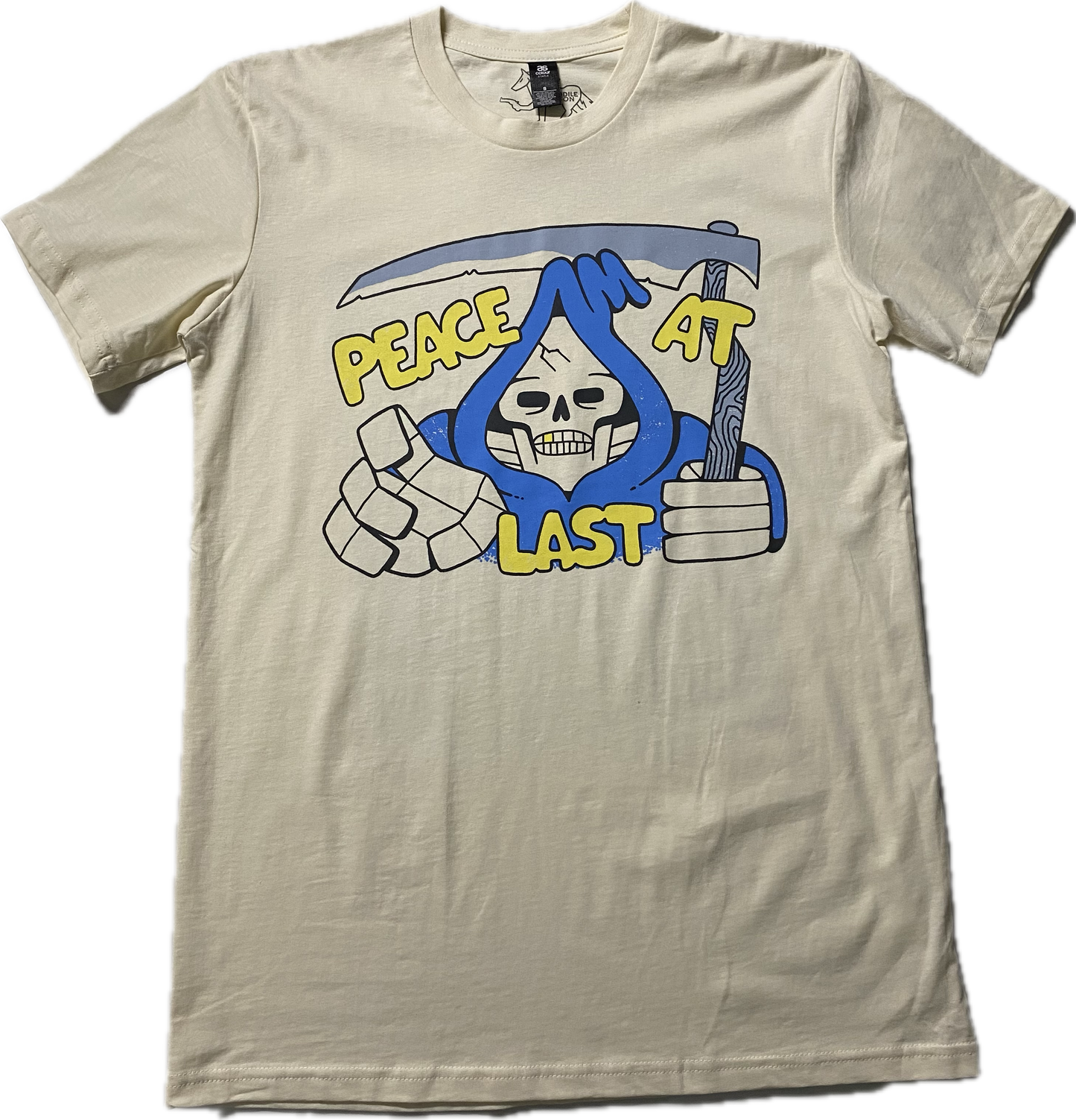 An off white t-shirt with a cartoon skeleton in a blue cloak printed on the chest area of the t-shirt. A sickle over the head of the skeleton and it reads Peach at Last in gold puffy font.