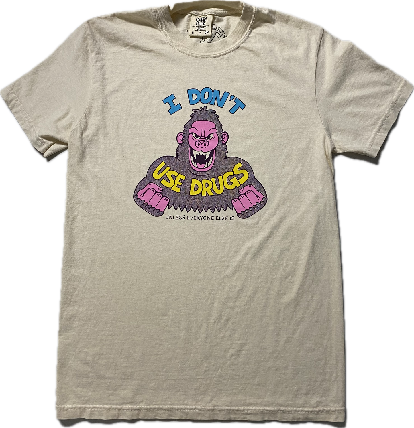 An off white short sleeve t-shirt with an angry purple cartoon gorilla with clinched fists and fangs.. It reads I Don't in blue font then Use Drugs in gold font. In tiny font at the bottom it reads Unless Everyone Else Is.