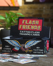 画像をギャラリービューアに読み込む, A black box of trading cards that reads Flash Friends Tatttoo Flash Trading Cards. The front side of the box has a cartoon eagle with wings spread. The box is on a wood table with some of the single cards spread out. Behind the box is a plant in a grey pot.