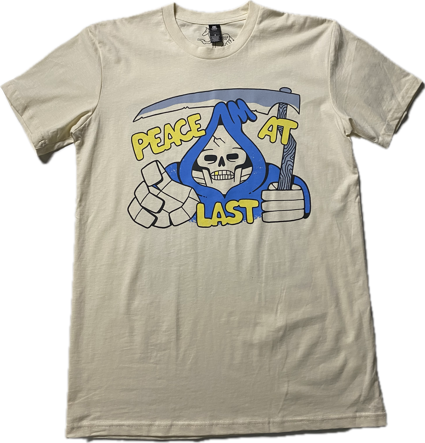 An off white t-shirt with a cartoon skeleton in a blue cloak printed on the chest area of the t-shirt.  A sickle over the head of the skeleton  and it reads Peach at Last in gold puffy font.