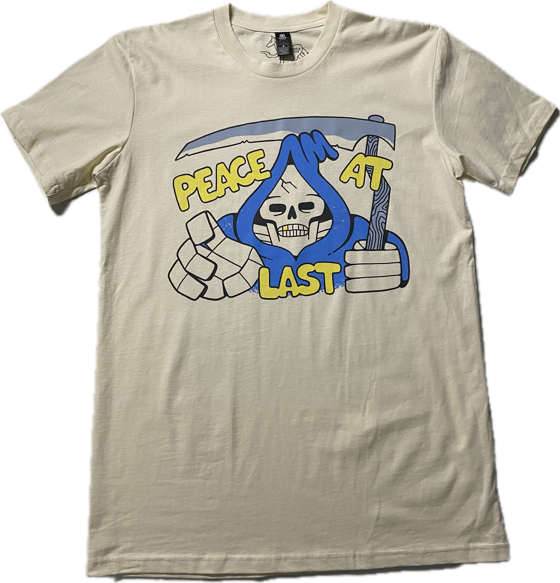 An off white t-shirt with a cartoon skeleton in a blue cloak printed on the chest area of the t-shirt.  A sickle over the head of the skeleton  and it reads Peach at Last in gold puffy font.