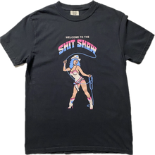 Load image into Gallery viewer, A black short sleeve t-shirt that reads Welcome to the Shit Show. The last 2 words are in a large font in rainbow colors of light blue, white and pink. Below the words is a cowgirl with blue hair in a white bathing suit and white boots. She is holding a blue lasso and have a holster with a pistol.
