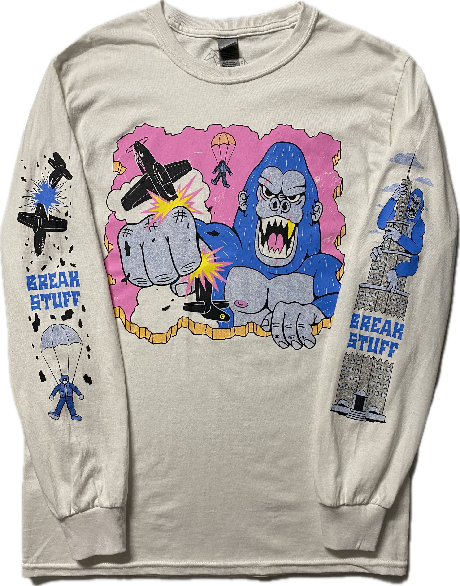 A white long sleeve t-shirt with a cartoon blue gorilla punching a black plane.  Behind the gorilla is the ejected pilot.  On the right sleeve it reads Break Stuff in blue font with a black broken plane above it and a parachuting pilot below it.  On the left sleeve is a blue gorilla climbing a high rise building and it reads Break Stuff too.