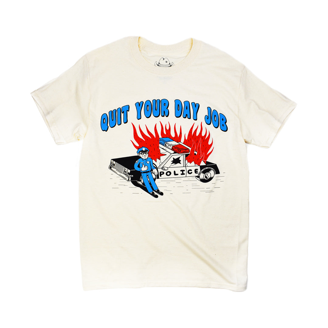 Cartoon flaming cop car on natural short-sleeve t-shirt that reads Quit Your Day Job in blue bubble font. Artist signature at the bottom right that reads Crocodile Jackson.