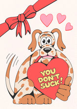 Cargar imagen en el visor de la galería, A Valentine&#39;s Day card that reads &quot;you don&#39;t suck&quot; in yellow font inside a red heart that a brown &amp; white spotted cartoon dog is holding.  Above the dog are 3 pink hearts.  On the left top corner is a red bow.
