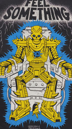 A video of the a black short sleeve tee that reads Feel something at the top with silver color and lighting around it. Below the words is a cartoon skull robot in gold that is strapped in an electric chair. Between it's feet is a gold mouse coming out of the bottom of the chair. Crocodile Jackson signature at the bottom.