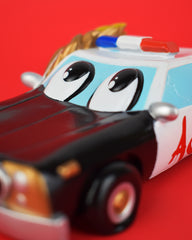 An introduction of a cartoon like black and white police car with googly eyes on the windshield and a gaping mouth as the grill containing 6 teeth (one of which is gold) and a tongue. The hub caps are yellow smiley faces and ACAB is spray painted in red on the white doors. The side windows are cracked and flames are flowing over the other side of the car.