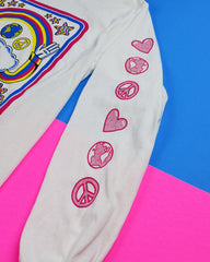 Close-up of shirt's sleeve. Descending down the sleeve vertically are drawings of a heart, the world, a peace sign, and this pattern repeats once more. The designs are all hot pink.