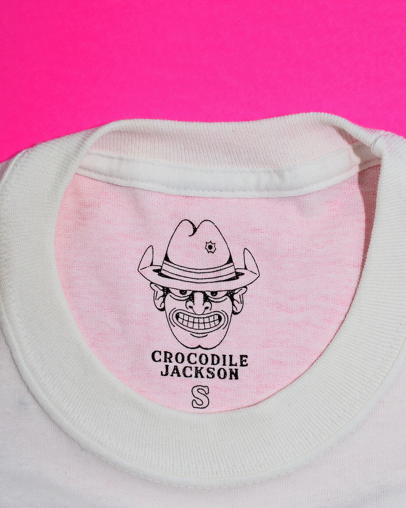 Close-up of this shirt's tag: the Crocodile Jackson cowboy logo, the words "Crocodile Jackson" in a western font below, and an outlined letter indicating size (in this case, the outline of an "S" for a size small shirt).