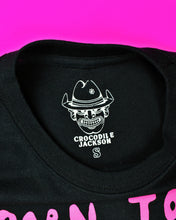 Cargar imagen en el visor de la galería, A black short sleeve t-shirt with Born to Raise Hell printed in a pink puffy font. There are 3 characters in a mid run pose below the wording. The first character is a pink devil with a black cape and thong. The 2nd character is a thief w/a black polka dot bandana, black eye mask, black/white striped long sleeve shirt, black pants and high top black sneakers. The 3rd character is a skeleton with a black robe, white socks and pink/white checkered sneakers.
