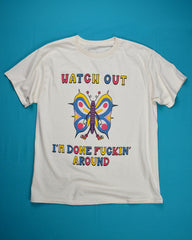A cartoon butterfly is in the center and it is wearing white gloves and red tennis shoes. It's wings are gold, blue and pink. Above the butterfly it reads Watch Out in alternating colors of pink, gold & blue. At the bottom it reads I'm Done Fuckin' Around also in the same alternating colors.