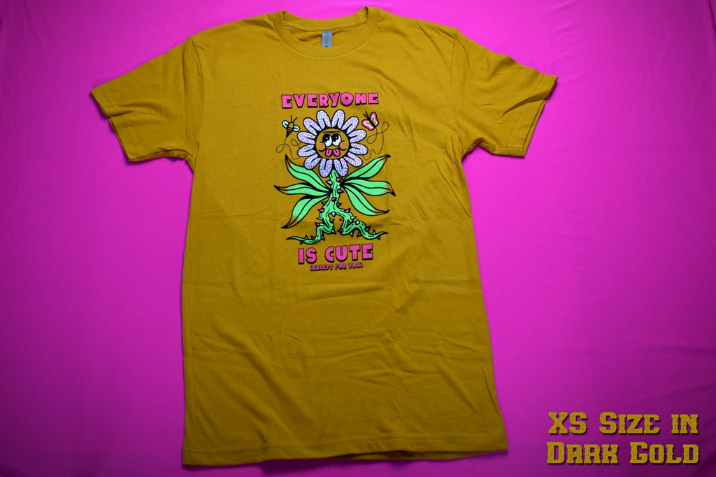 Dark gold short sleeve t-shirt that reads Everyone is Cute (except for you) in pink font. The (except for you) is in a very small font. In the center is a large flower with a thorny green stalk and 6 flailing leaves. The flower petals are blue, pink and white polka dots and the yellow center of the flower has googly eyes round cheeks and a pink double tongue sticking out. On either side of the top of the flower is a flying bee and butterfly.