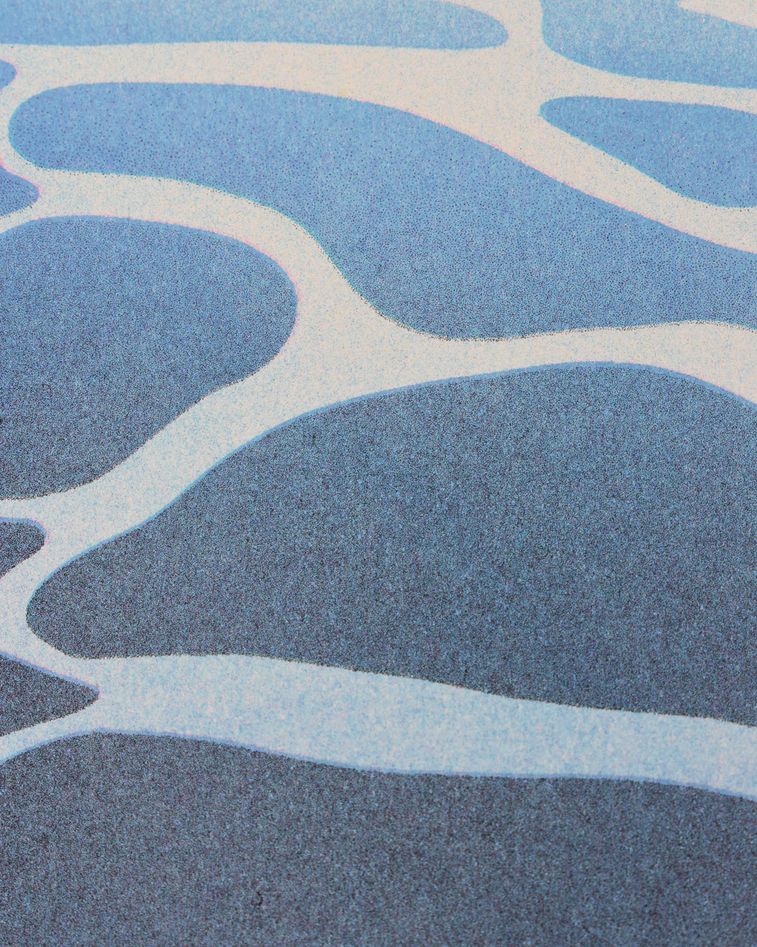 Closeup of the risograph print. The focus is on the ocean, showing the gradient of the water from a dark blue on the bottom of the print to a lighter blue on the top, a layer of sea foam on top of all the water, and a grainy effect across everything.
