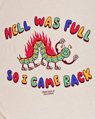 Close up of a cream colored t-shirt that reads Hell Was Full at the top and So I Came Back at the bottom in alternating red, yellow, green and blue colored letters. The center is a a smiling cartoon inch worm with 6 legs and tennis shoes for its feet. The top of the worm has flames shooting up and it has two arms in the air showing off its muscles.