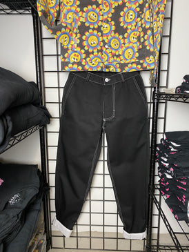 A picture of a black pair of pants (front view) hung on a black wire mesh background.  The top stitching is white as well as the button.  The cuffs are rolled up to show the white fabric underneath.