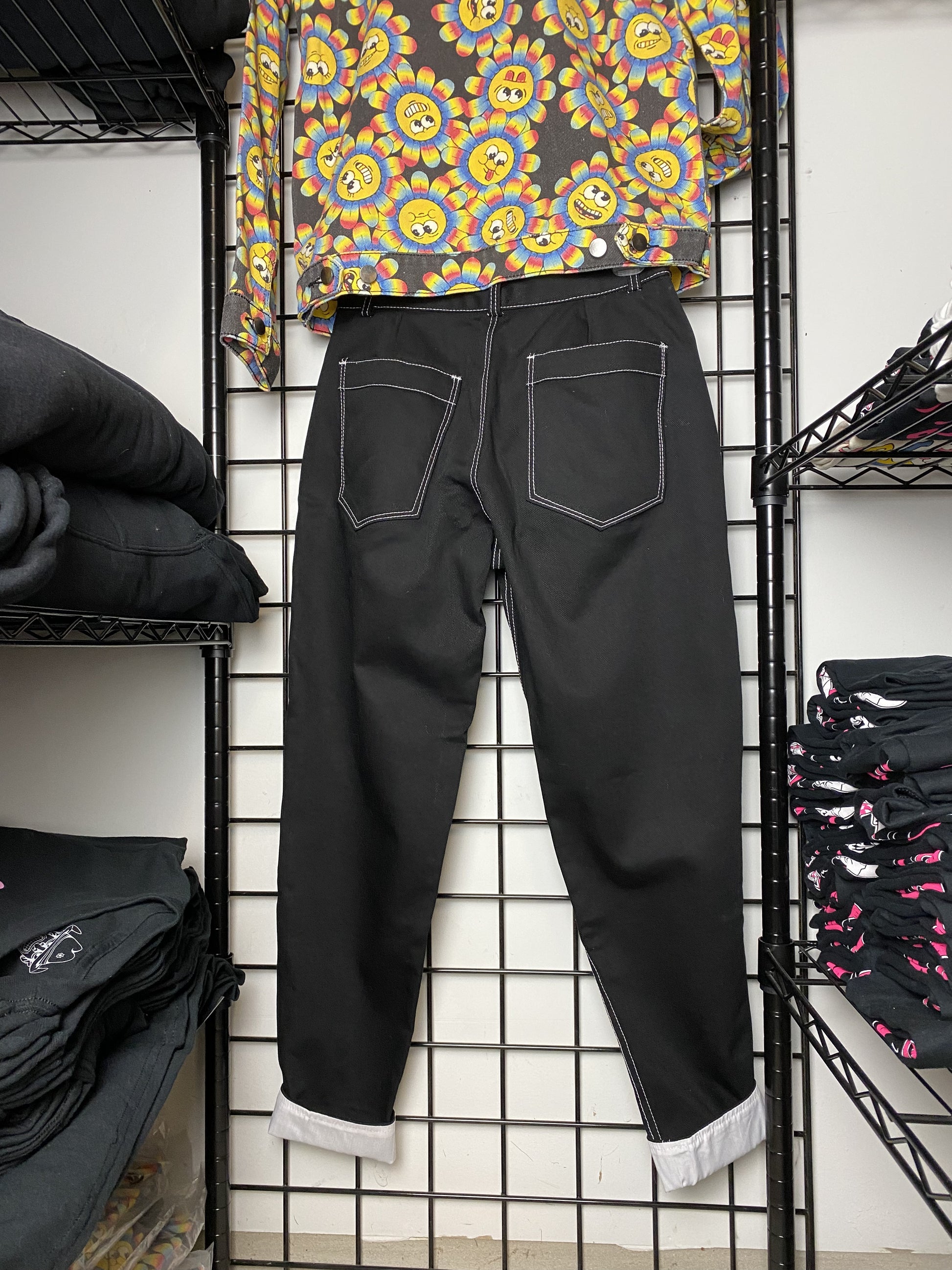 A picture of a black pair of pants (back view) hung on a black wire mesh background.  The top stitching is white as well as the button.  The cuffs are rolled up to show the white fabric underneath.