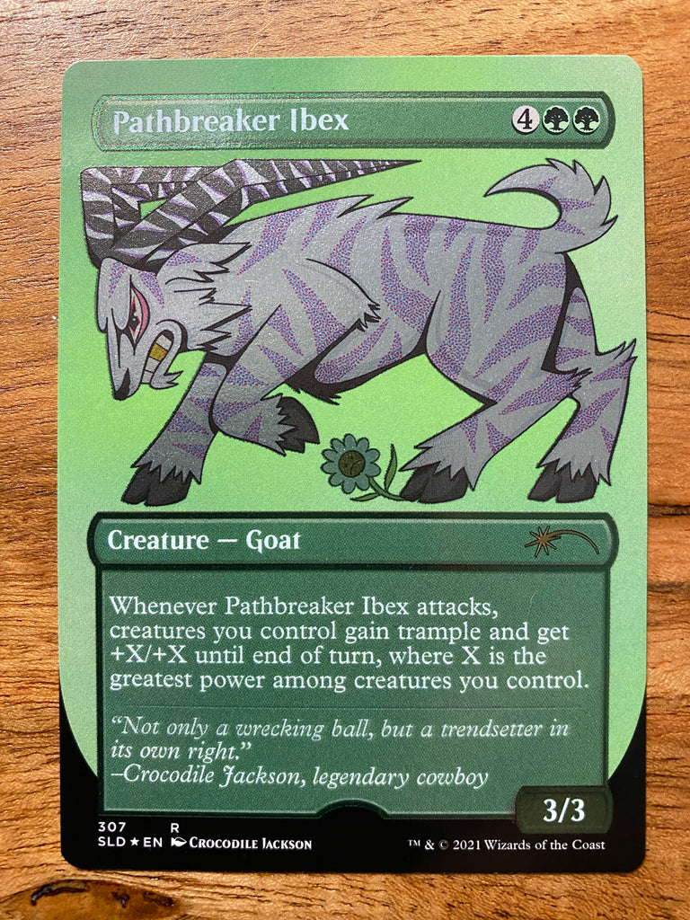 A trading card on a wood table that shimmers in the light.  The card title is Pathbreaker Ibex and it has a cartoon goat like creature in a charging position.  The ibex is white with purple zebra like stripes.  It's long horns are striped black and white.  At the feet of the goat is a flower with a sad face.  Below the ibex is information about the game this card pertains to - Magic the Gathering:  Secret Lair.