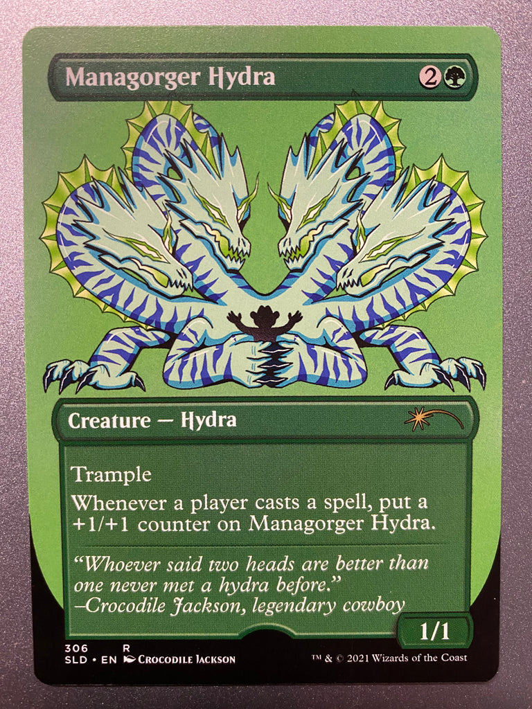 Trading card with a title at the top left that reads Managorger Hydra.  Below that is a cartoon creature with 4 heads all pointing down to a silhouette of a man in a cowboy had that is trapped in it's claws.  The creature is white with purple stripes, gold mane and black claws.  At the bottom of the card information about the creature and the game - Magic the Gathering.
