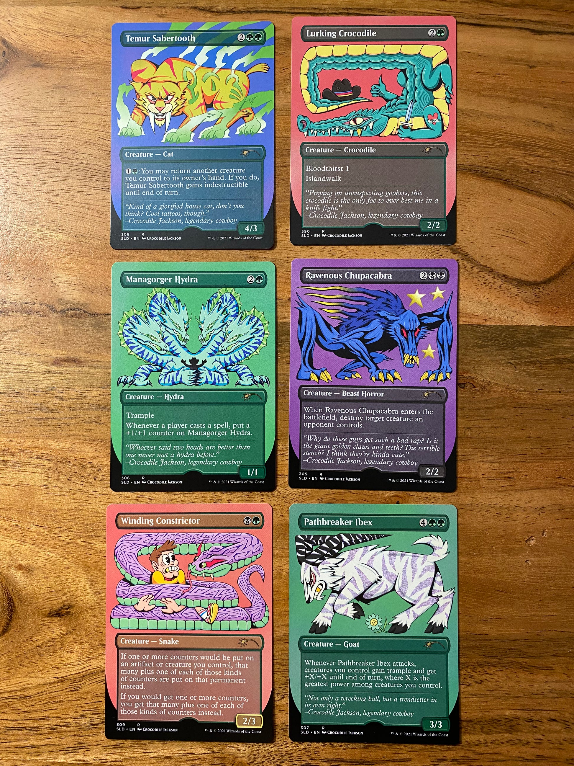 A set of 6 trading cards on a wood table.  Each card has a cartoon animal and are part of the Magic the Gathering Secret Lair game by Hasbro.
