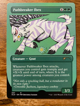 A trading card on a wood table.  The card title is Pathbreaker Ibex and it has a cartoon goat like creature in a charging position.  The ibex is white with purple zebra like stripes.  It's long horns are striped black and white.  At the feet of the goat is a flower with a sad face.  Below the ibex is information about the game this card pertains to - Magic the Gathering:  Secret Lair.