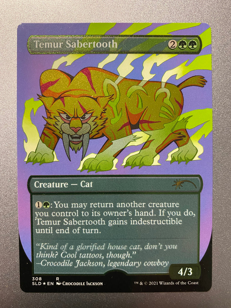 A shimmering trading card titled Temur Sabertooth.  In the center is a yellow cartoon lion with very large fangs looking straight ahead.  There are green symbols on its body and green lightning bouncing off its feet and body.  At the bottom is information about the card and a quote from the artist - Crocodile Jackson.