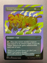 Load image into Gallery viewer, A shimmering trading card titled Temur Sabertooth.  In the center is a yellow cartoon lion with very large fangs looking straight ahead.  There are green symbols on its body and green lightning bouncing off its feet and body.  At the bottom is information about the card and a quote from the artist - Crocodile Jackson.
