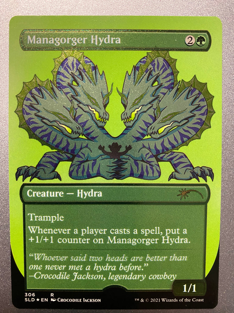 A shimmering trading card with a title at the top left that reads Managorger Hydra.  Below that is a cartoon creature with 4 heads all pointing down to a silhouette of a man in a cowboy had that is trapped in it's claws.  The creature is white with purple stripes, gold mane and black claws.  At the bottom of the card information about the creature and the game - Magic the Gathering.