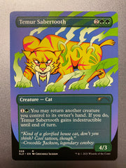 A trading card titled Temur Sabertooth.  In the center is a yellow cartoon lion with very large fangs looking straight ahead.  There are green symbols on its body and green lightning bouncing off its feet and body.  At the bottom is information about the card and a quote from the artist - Crocodile Jackson.