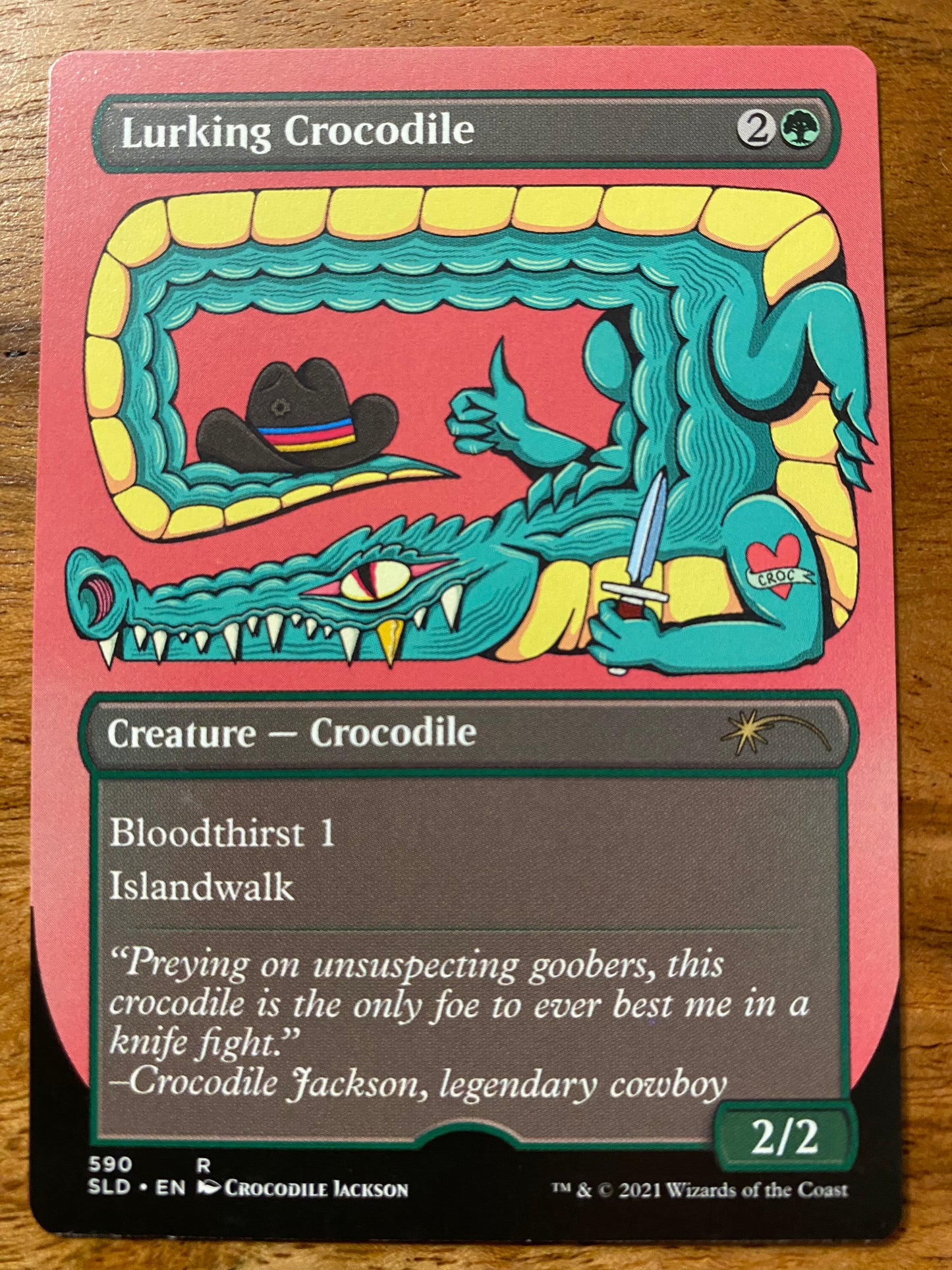 A trading card with a title of Lurking Crocodile.  Below the title is a cartoon crocodile with his tail overhead and a cowboy hat sitting on the end of it's tail.  The left arm of the crocodile is holding a knife and has a heart tattoo that reads 'Croc' on the top of it's arm.  Below the art is information on the Magic the Gathering game.
