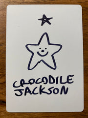 The back of the trading card that is all white and it has a hand drawn star with a smiley face and the artist signature in black marker.