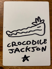 The back of the trading card that is all white with a hand drawn crocodile head with the artist signature below - Crocodile Jackson - in black marker.