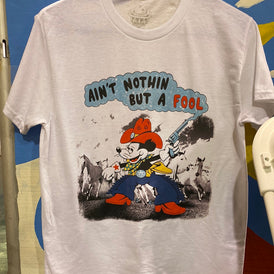 A white short sleeve t-shirt with a cartoon cowboy mouse printed on the front.  The mouse has a large red cowboy hat, blue chaps and red boots.  It is also wearing white gloves with a red star.  It's left had has a pistol pointing upwards.  The background has 4 white horses in stampede.  Above the mouse it reads Ain't Nothin But a Fool in puffy black and red letters.